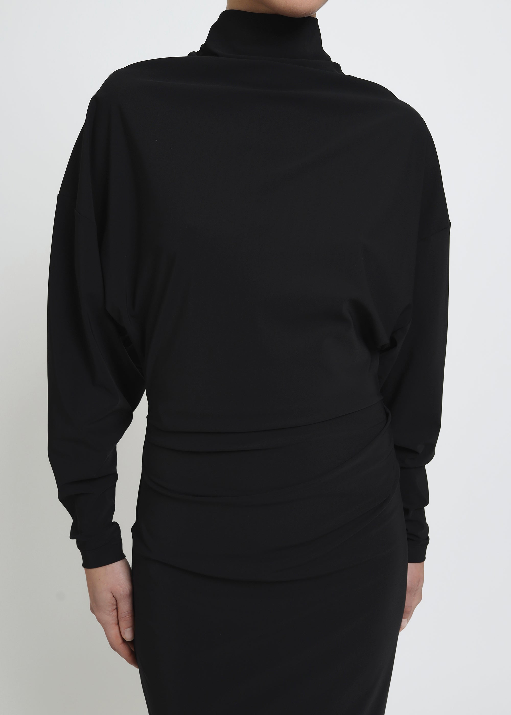 A long-sleeved black mock-neck midi dress with a draped waist.