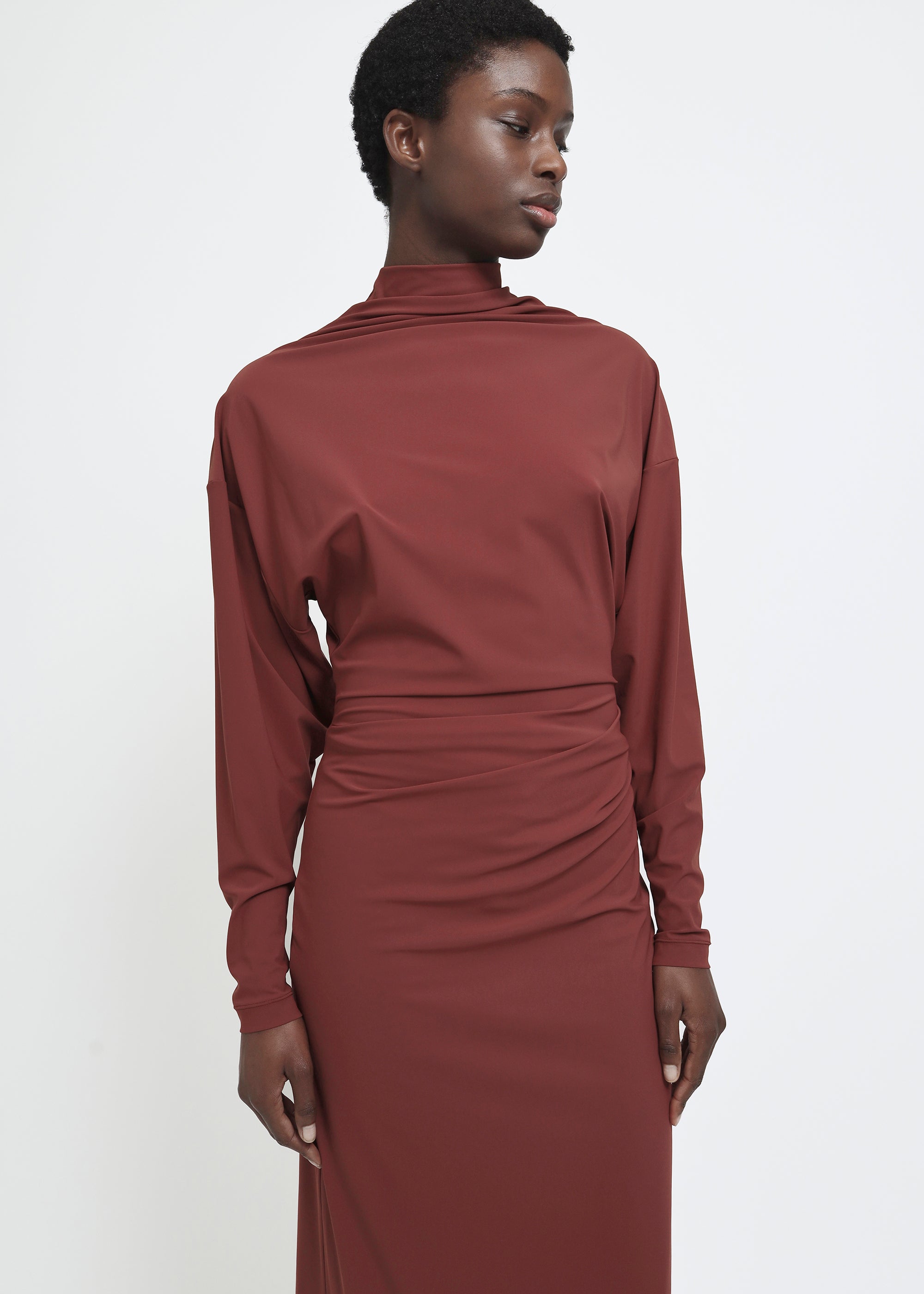 A long-sleeved, high-neck maxi dress in a muted terracotta or rust red color.