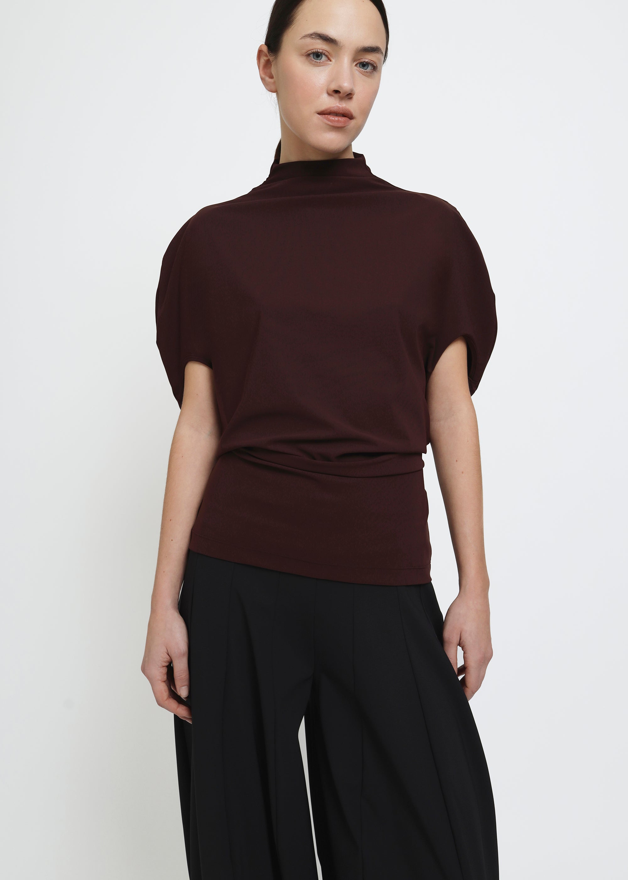 A dark brown burgundy short-sleeve mock neck top with puffed circle sleeves and a gathered, draped waist detail.