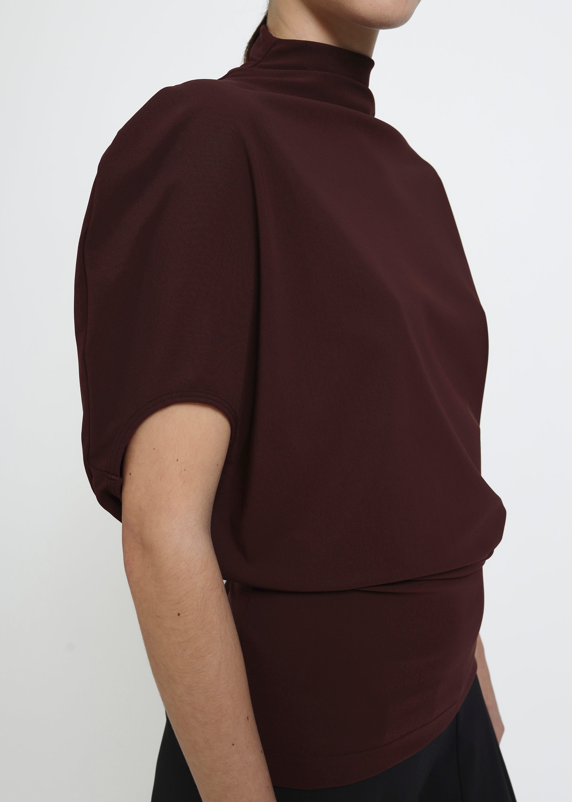 A dark brown burgundy short-sleeve mock neck top with puffed circle sleeves and a gathered, draped waist detail.