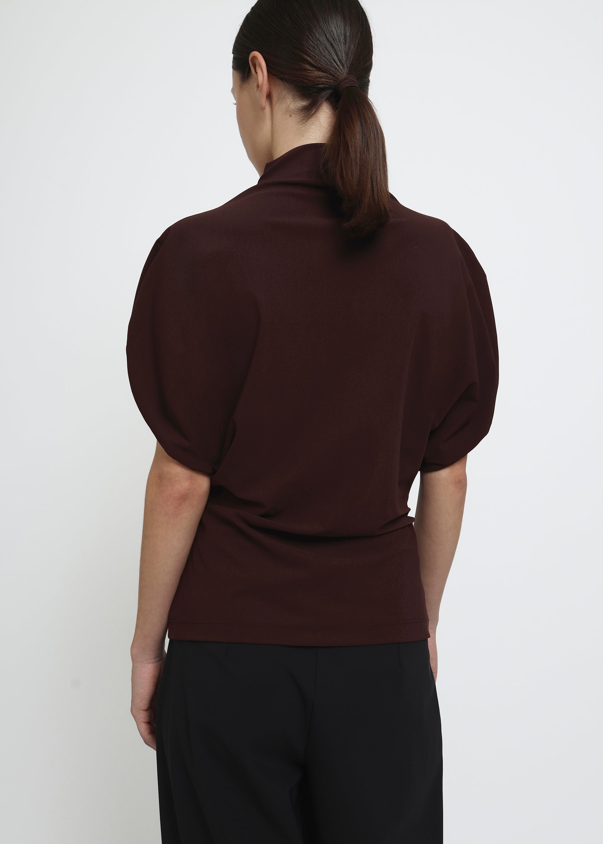 A dark brown burgundy short-sleeve mock neck top with puffed circle sleeves and a gathered, draped waist detail.