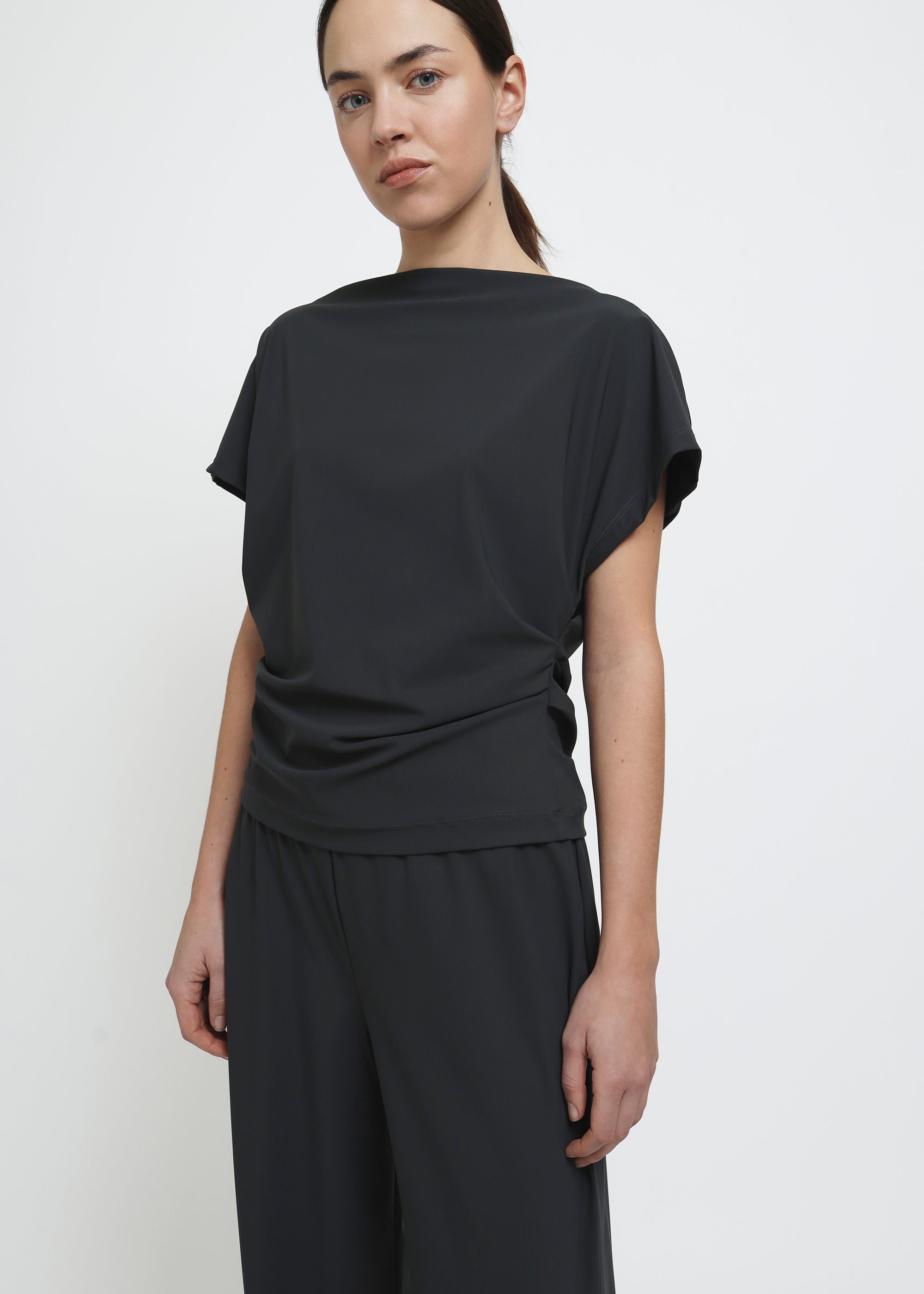 A dark grey short-sleeve top with draped fabric and a gathered waist detail.