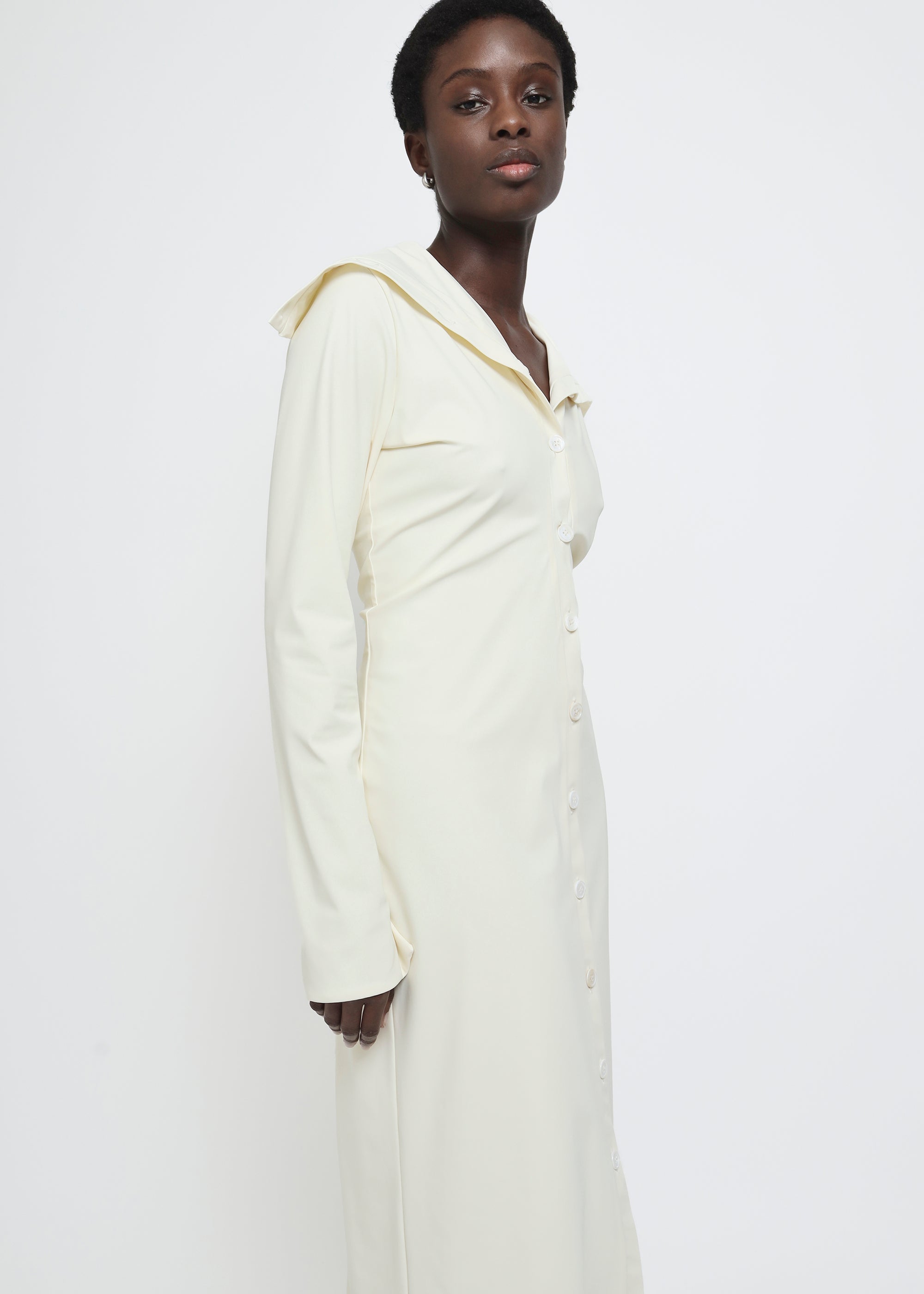A long-sleeved cream-colored button-up dress with a wide collar.