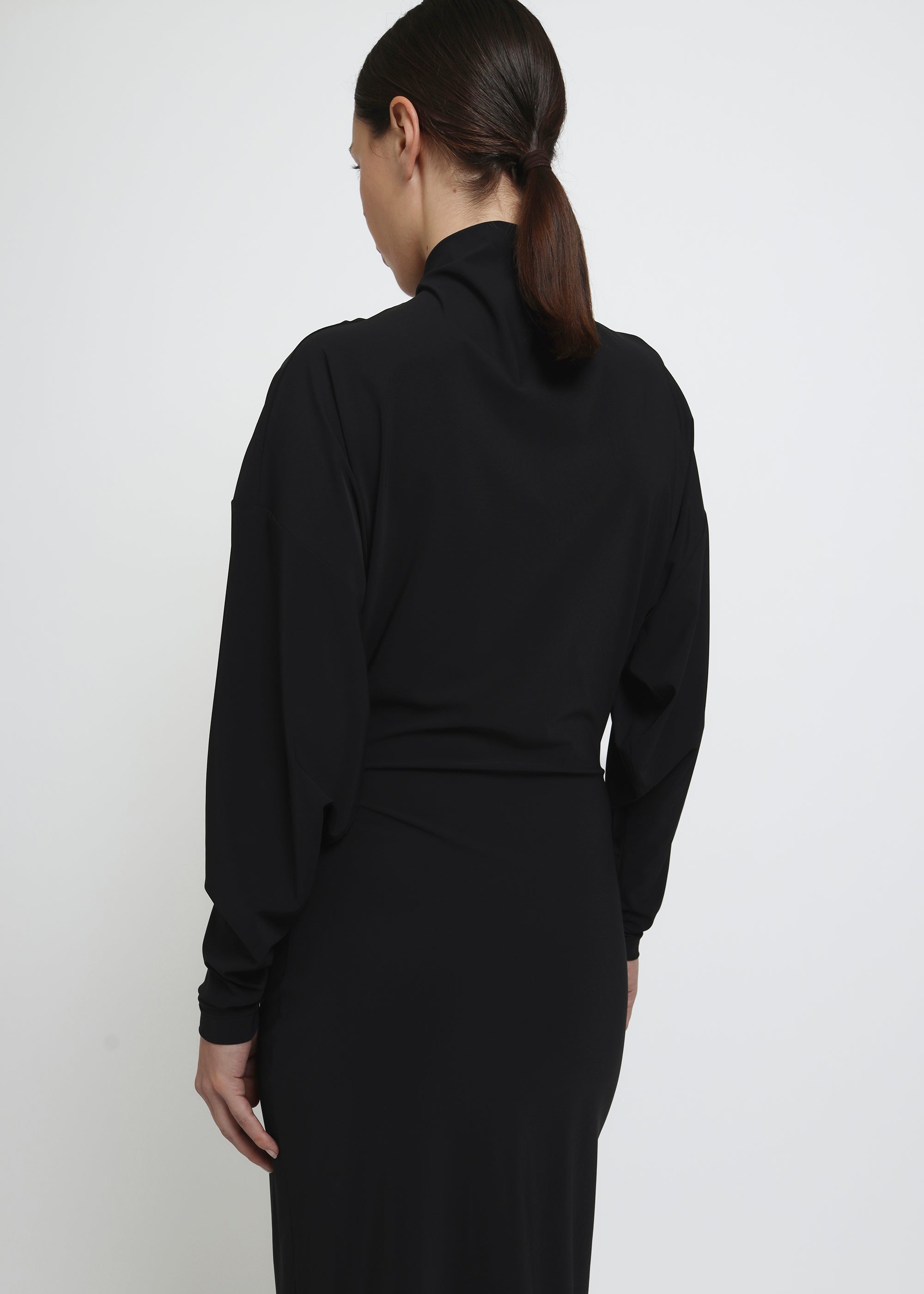 A long-sleeved black mock-neck midi dress with a draped waist.