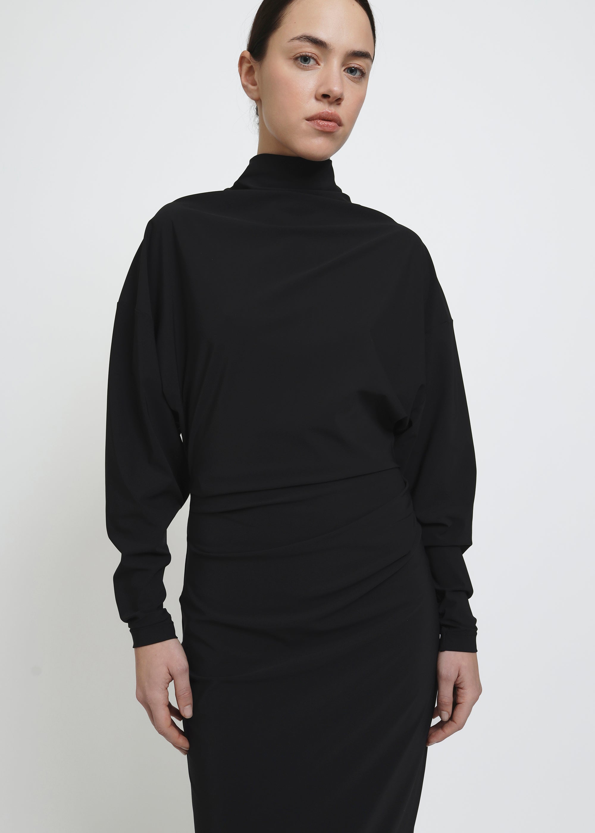 A long-sleeved black mock-neck midi dress with a draped waist.