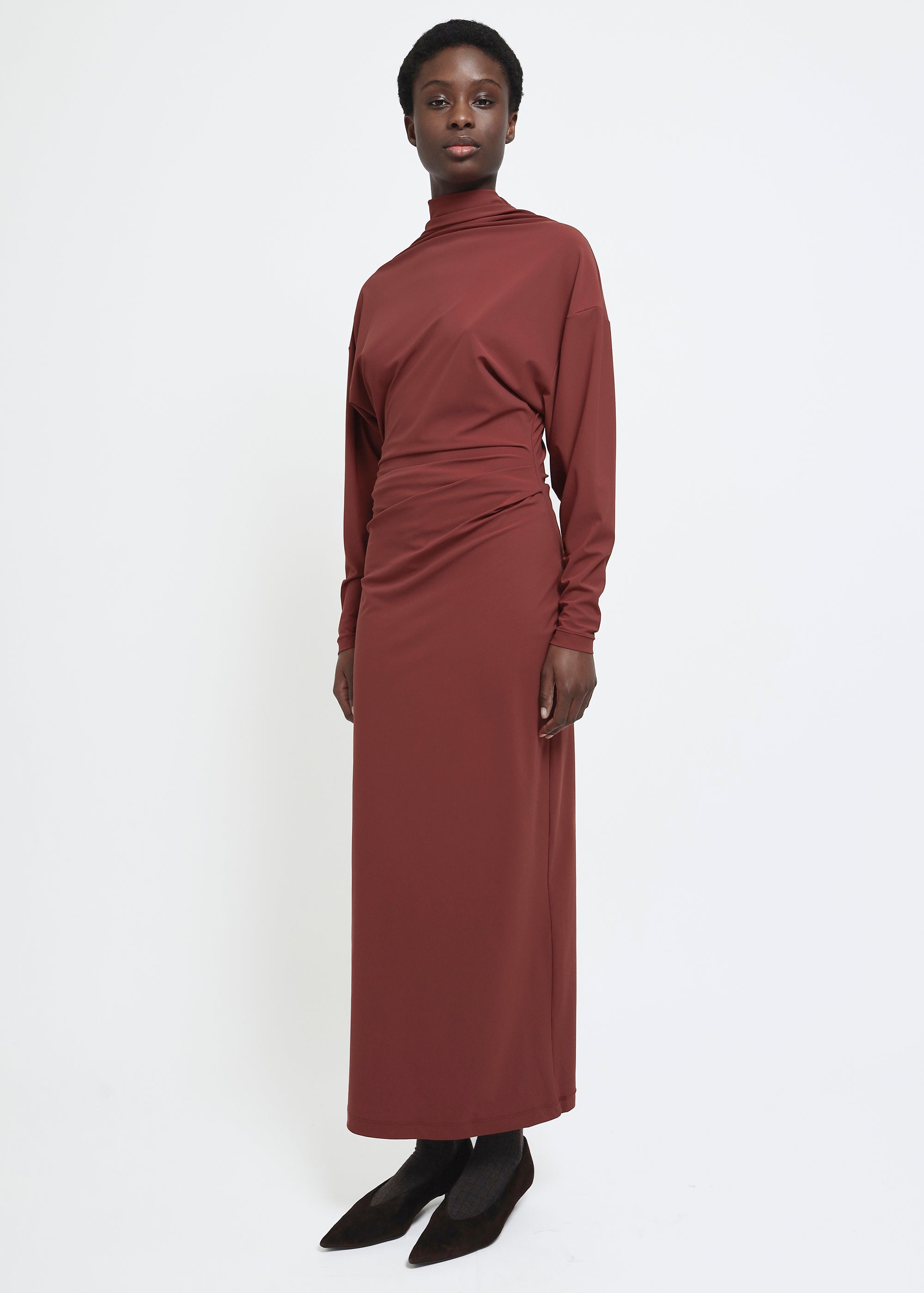 A long-sleeved, high-neck maxi dress in a muted terracotta or rust red color.