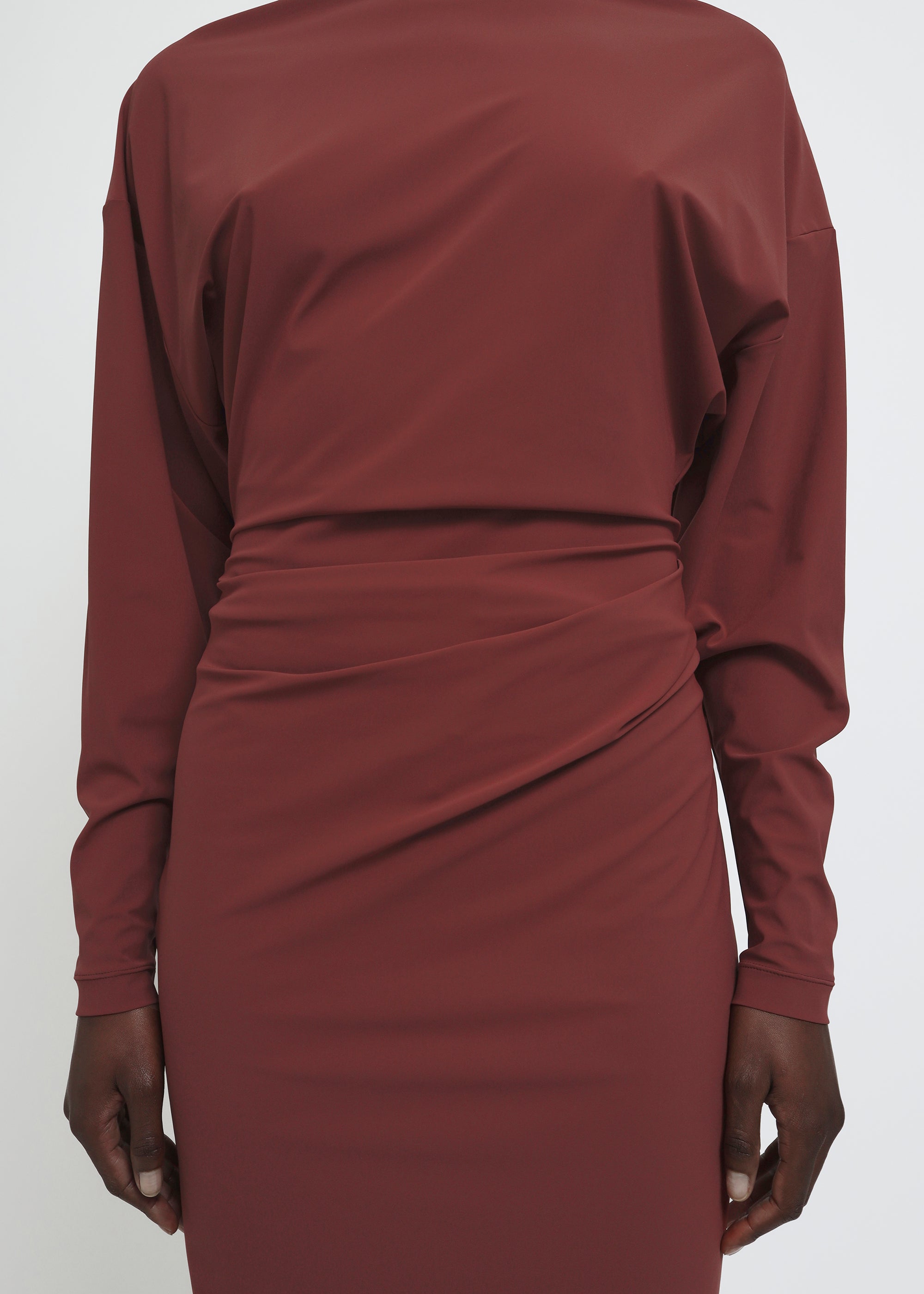 A long-sleeved, high-neck maxi dress in a muted terracotta or rust red color.