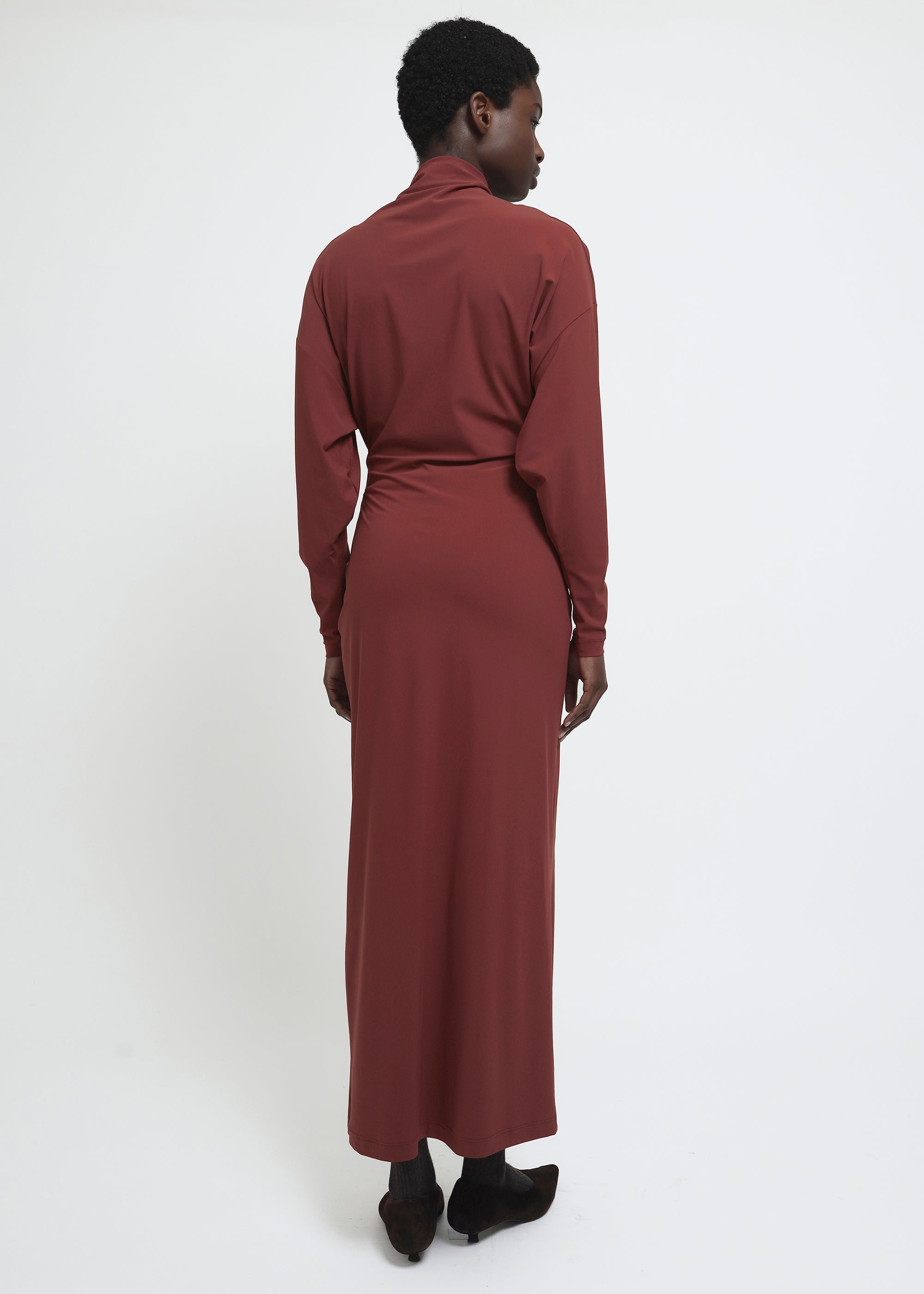 A long-sleeved, high-neck maxi dress in a muted terracotta or rust red color.