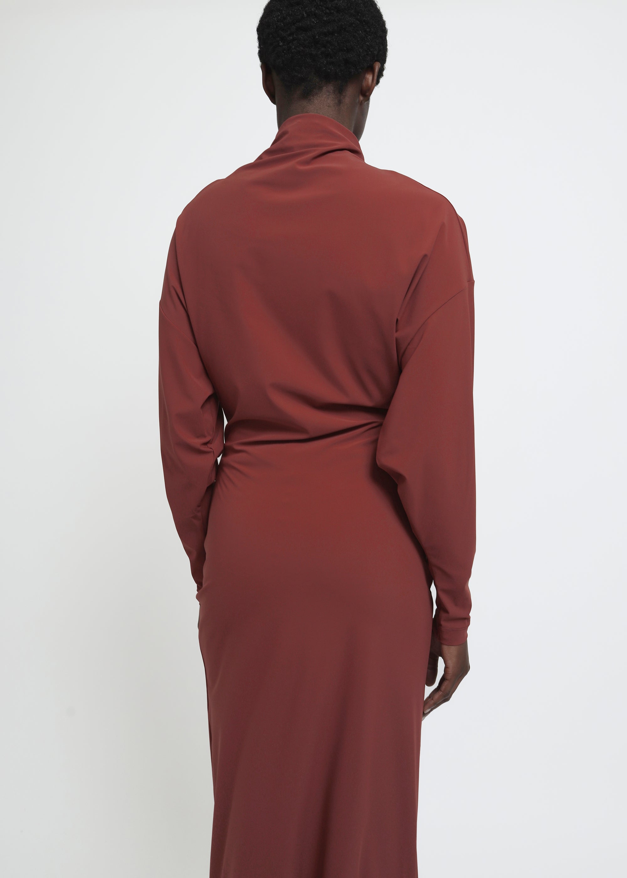 A long-sleeved, high-neck maxi dress in a muted terracotta or rust red color.