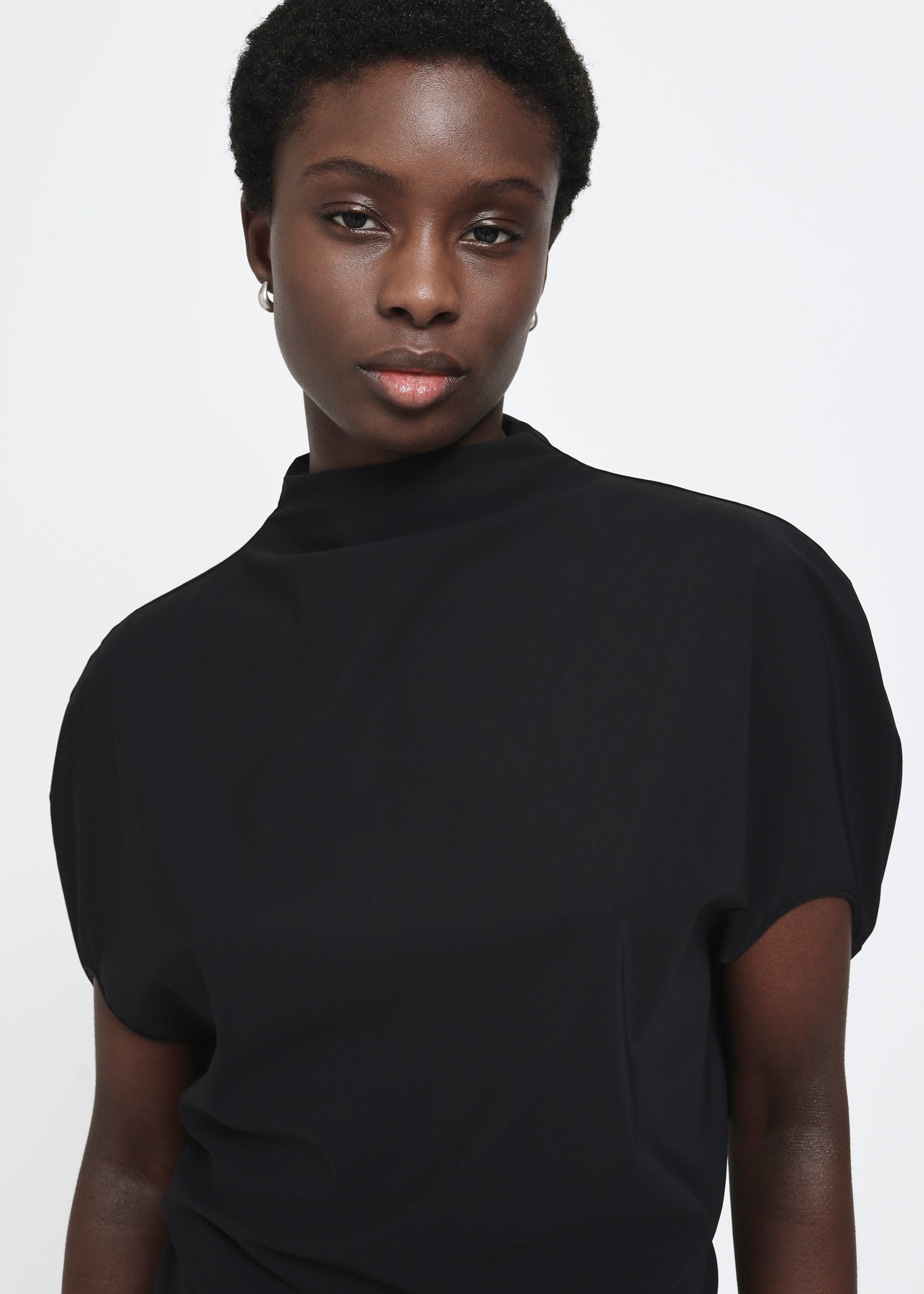 A black short-sleeve mock neck top with puffed circle sleeves and a gathered, draped waist detail.