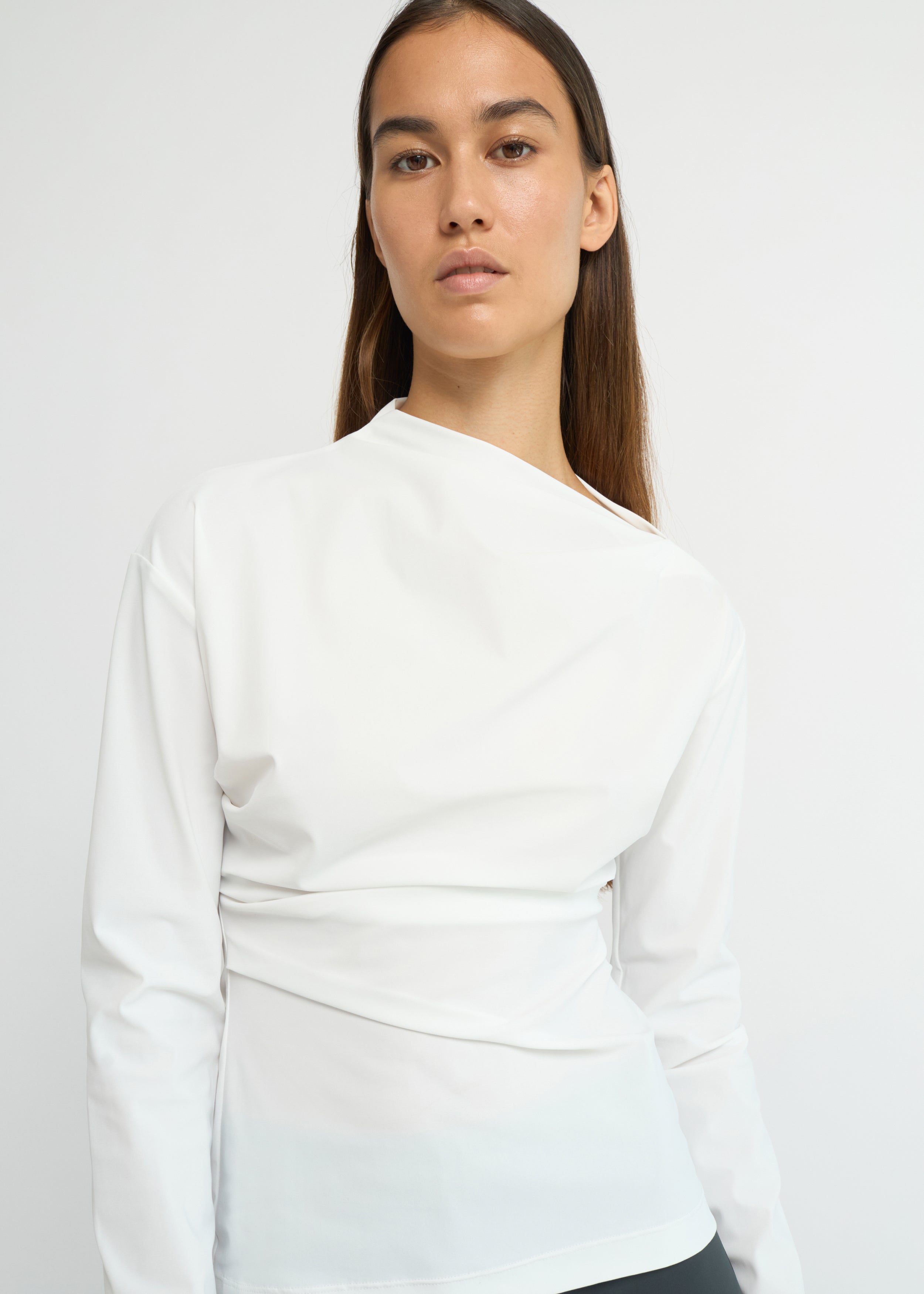 Off-white long-sleeve top with an asymmetrical neckline and soft waist folds